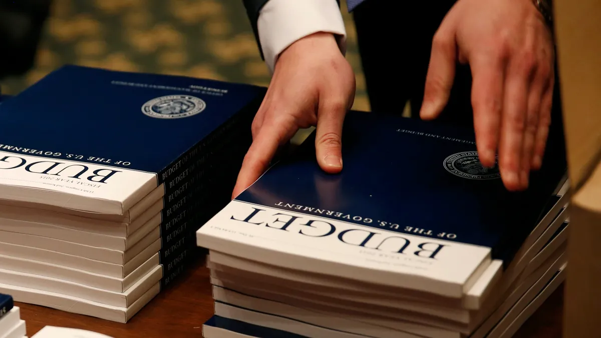 A man straightens up a stack of booklets titled "Budget of the U.S. Federal Government." 