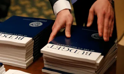 A man straightens up a stack of booklets titled "Budget of the U.S. Federal Government." 